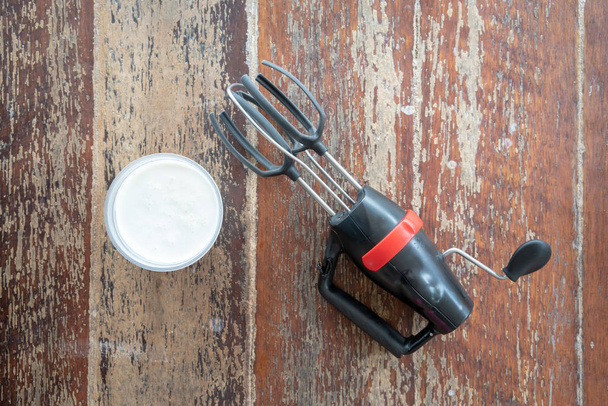 Agitador manual negro y rojo con crema batida para mantequilla casera sobre fondo de madera
. - Foto, imagen