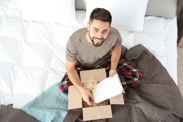 Young man opening parcel in bedroom at home - Photo, Image