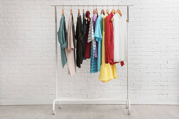 Wardrobe rack with stylish clothes near brick wall indoors - Fotoğraf, Görsel