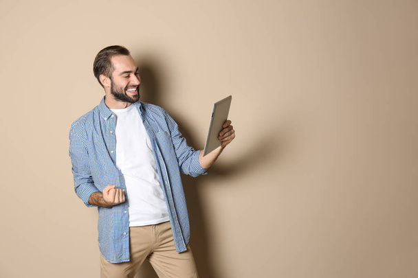 Emotional young man with tablet celebrating victory on color background. Space for text - Fotografie, Obrázek