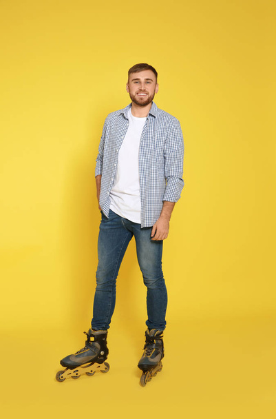 Full length portrait of young man with inline roller skates on color background - Foto, afbeelding