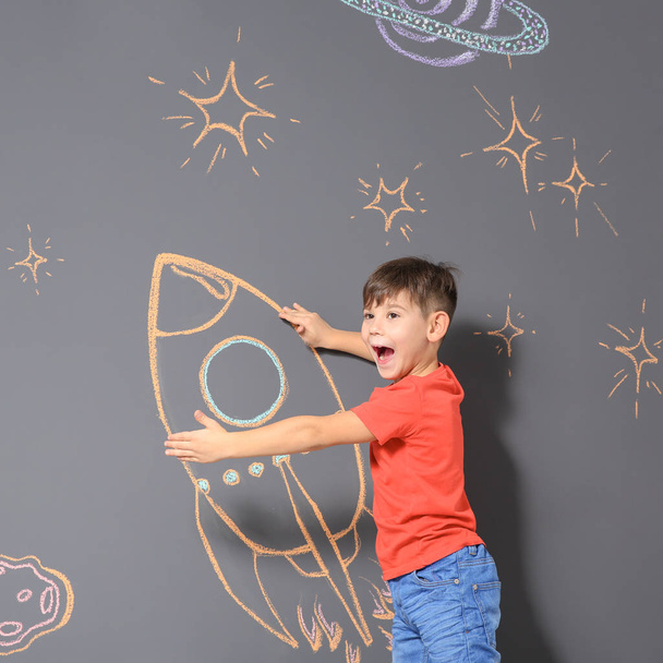 Cute little child playing with chalk rocket drawing on grey background - Fotoğraf, Görsel