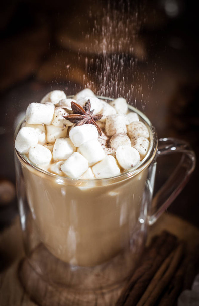 Hot coffee with milk in a glass with double walls with marshmallow, anise star and falling cacao powder. Brown, Selective focus - Fotografie, Obrázek