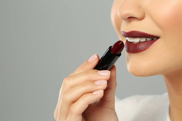 Beautiful woman applying dark lipstick on gray background, closeup. Space for text - Фото, изображение