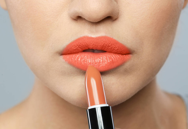 Young woman wearing beautiful lipstick on color background, closeup - Foto, Imagen