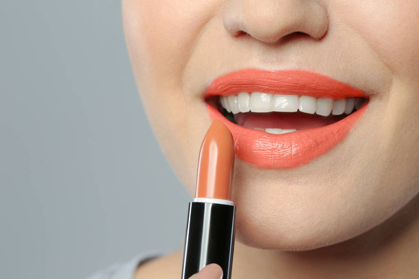 Young woman applying beautiful lipstick on gray background, closeup - Фото, зображення
