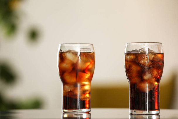 Glasses of cola with ice on table against blurred background - Фото, зображення