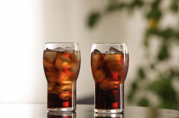 Glasses of cola with ice on table against blurred background - Foto, Imagem