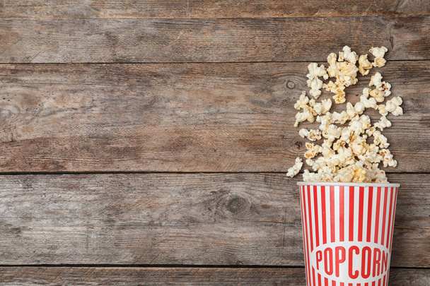 Overturned paper cup with tasty popcorn on wooden background, top view. Space for text - 写真・画像