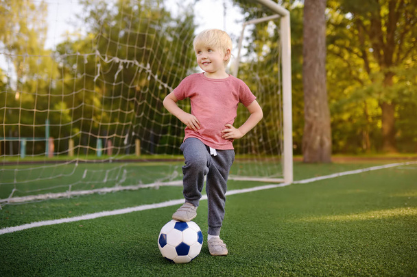 Little boy having fun playing a soccer/football game on summer day. Active outdoors game/sport for children. Kids soccer classes and camps - Photo, image