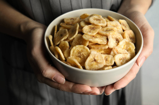 Woman holding bowl with sweet banana slices on light background, closeup. Dried fruit as healthy snack - Photo, Image