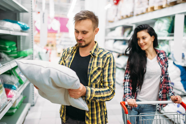 Happy couple buying pillow in supermarket. Male and female customers on family shopping. Man and woman purchasing goods for the house - Foto, Imagem