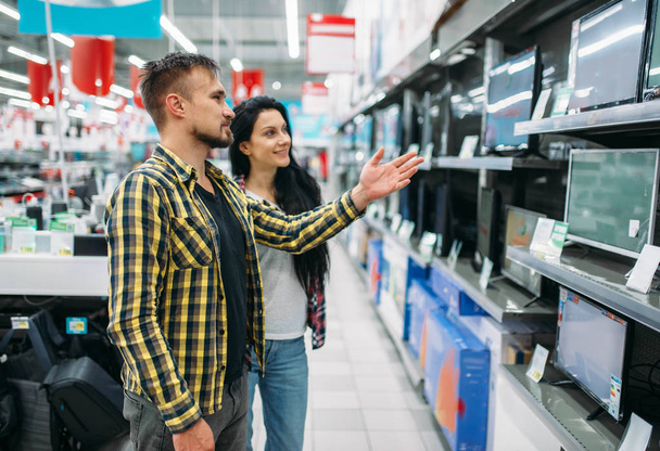 Молодая пара покупает монитор в супермаркете. Мужчины и женщины покупают семейные товары. Мужчина и женщина покупают товары для дома
 - Фото, изображение