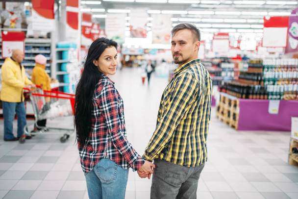 Young couple hold hands in supermarket, back view. Male and female customers on family shopping. Man and woman purchasing in hypermarket - Photo, Image