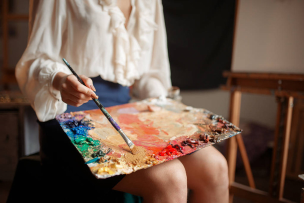 Female painter holds color palette and brush in studio. Creative paintbrush art, artist drawing in class, workshop interior on background - Photo, Image