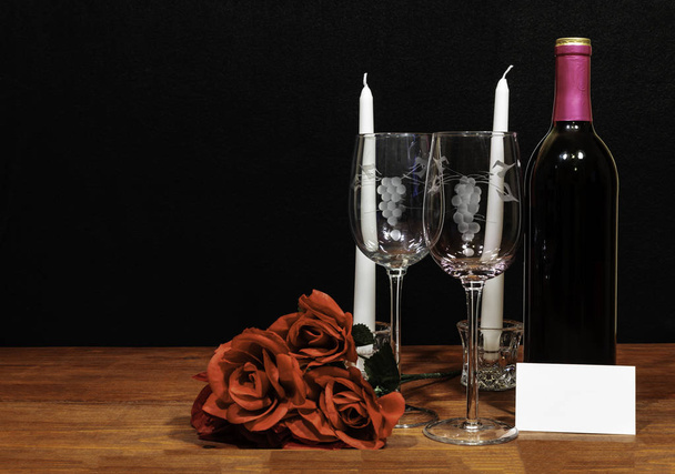 Krásné leptaný vinné sklenice a láhev červeného vína, bílé svíčky a červené růže na dřevěný stůl s názvem značky na tmavém pozadí. Valentýna, matky den, Velikonoce, Vánoce, svatbu pojmy - Fotografie, Obrázek