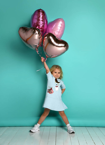little girl has fun with a bunch of pink air balloons in the shape of her heart. - Foto, immagini