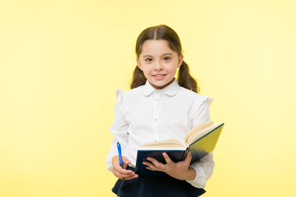 Child girl school uniform clothes hold book and pen. Girl cute write down idea notes. Notes to remember. Write essay or notes. Personal schedule. Making notes. Child school uniform kid doing homework - Foto, immagini