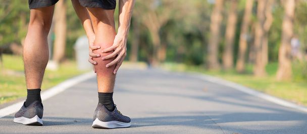 Young fitness man holding his sports leg injury. muscle painful during training. Asian runner having calf ache and problem after running and exercise outside morning. sport and healthy concepts - Photo, Image