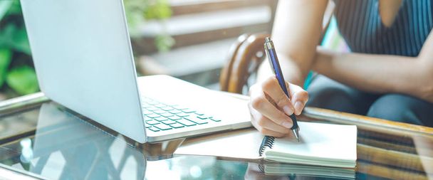 La mano de la mujer de negocios está escribiendo en un bloc de notas con un bolígrafo y utilizando un ordenador portátil.Banner web
. - Foto, Imagen