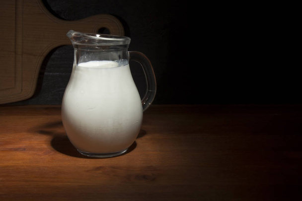 Glass jug with fresh milk on a wooden table - Foto, Imagen