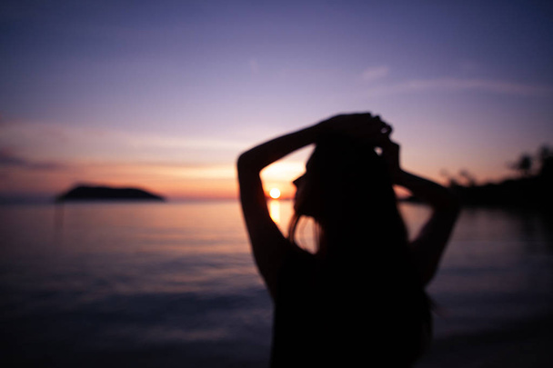 Bulanık arka plan. Parlak renkli günbatımı bir arka planda bir tropikal plajda güzel bir ince genç kadın silüeti - Fotoğraf, Görsel