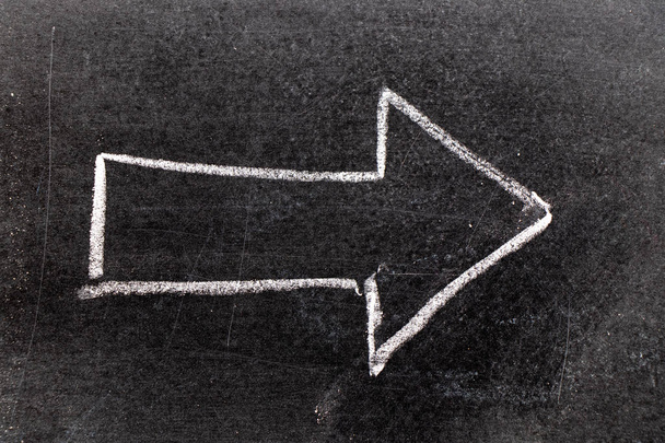 Wit krijt hand in pijlshape puttend uit zwarte bord achtergrond - Foto, afbeelding