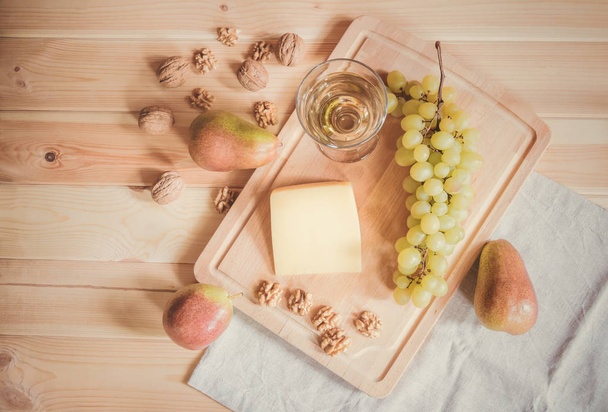 Glas Weißwein, Parmesan, Walnüsse, Birnen und Traubenzweig auf Holztisch. Ansicht von oben. Getöntes Image. - Foto, Bild