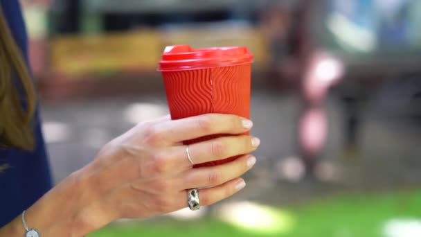 Женщина на улице держит красную пластиковую чашку в руке
. - Кадры, видео