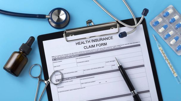 Formulario de reclamo de seguro de salud con pluma sobre fondo azul
 - Foto, Imagen