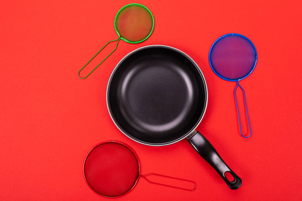 Frying pan in the center with cooking utensils around isolated on red background - Fotoğraf, Görsel