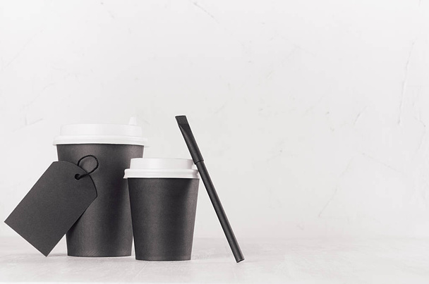 Coffee mockup - big, small black paper cups with white caps, blank label and sugar bag on white wood table with copy space, coffee shop interior. Modern elegant concept for branding identity, advertising, design. - Fotografie, Obrázek