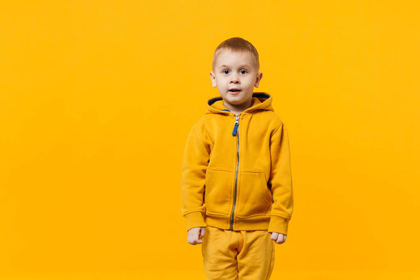 Little cute kid boy 3-4 years old wearing yellow clothes isolated on bright orange wall background, children studio portrait. People sincere emotions, childhood lifestyle concept. Mock up copy space - Foto, imagen