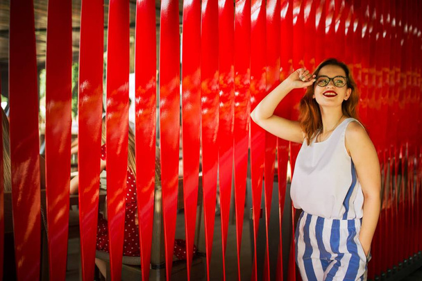 Attractive redhaired woman in eyeglasses posing against red background. - Fotó, kép