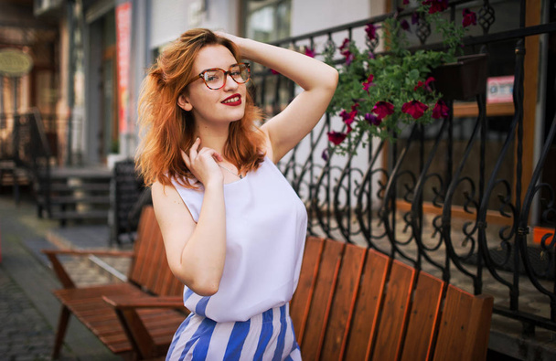 Attractive redhaired woman in eyeglasses posing at street of spring city. - Φωτογραφία, εικόνα