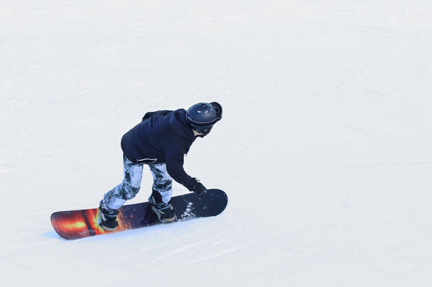 Snowboarder, der auf einem Snowboard den schneebedeckten Hang eines Skigebiets hinunterfährt. Wintersport. Freestyle und Slalomabfahrt. Ausrüstung für extreme Kälte. Aktivität für Gesundheit in der Kälte. Jugendhobby - Foto, Bild