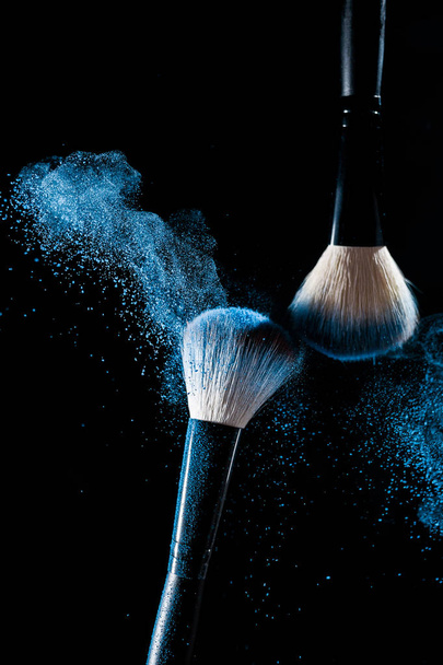 Two brushes for makeup with blue make-up shadows in motion on a black background - Photo, image