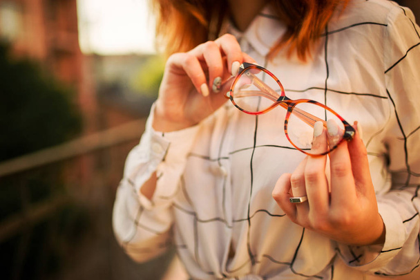 Close up photo of eyeglasses holding redhaired  woman, wear white blouse. - Foto, Bild