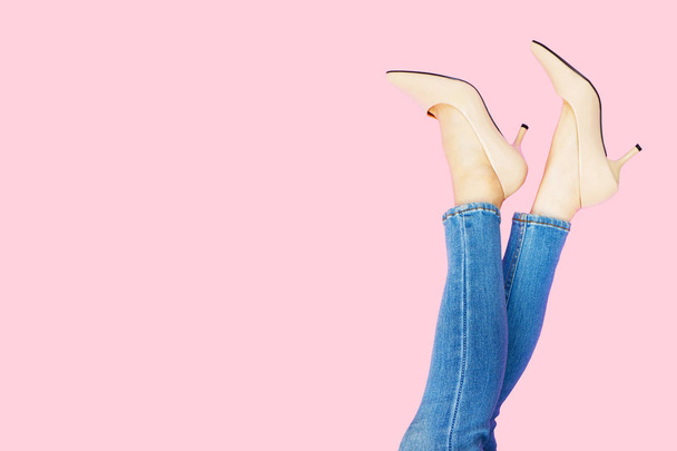 Beautiful Woman Feet & Slim Legs in Beige Medium High Heels on Pastel Pink. Portrait of Sexy Legs. Young Female Wearing Jeans (Blue Pants) in Stylish Shoes Raised Up Isolated on Pink Color Background. - Fotó, kép