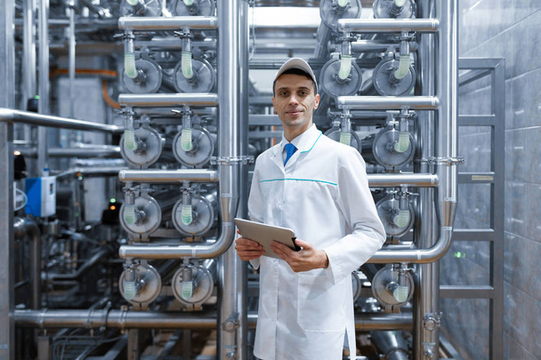Mann in weißem Gewand mit Tablette in der Hand steht in der Fabrik - Foto, Bild