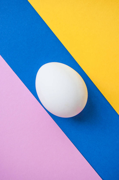 Fehér egy tojást a sötét kék, világos rózsaszín és sárga háttér előtt copyspace. - Fotó, kép