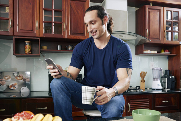Позитивний молодий чоловік п'є ранкову каву та друзів з смс
 - Фото, зображення