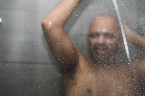 Brittiläinen aasialainen mies suihkussa suihkukaapissa kopiotilaa. Kalju keski-ikäinen mies suihkussa. Kasvojen ilmeitä voidaan käyttää välittämään tunteita, kuten surua, huolta, masennusta ja yksinäisyyttä.
.  - Valokuva, kuva