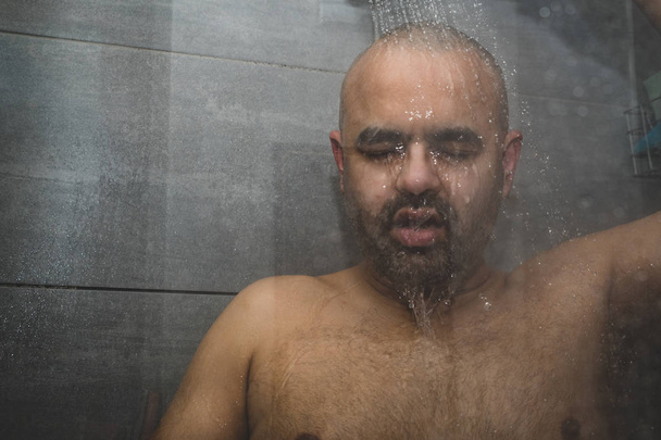 Британський азіатських людині приймаючи душ в душову кабіну - копія простору. Лисий середнього старшими людина в душова кабінка, приймаючи душ. Міміку можуть бути використані для передачі відчуття, такі, як смуток, занепокоєння, депресії і Самотність.  - Фото, зображення