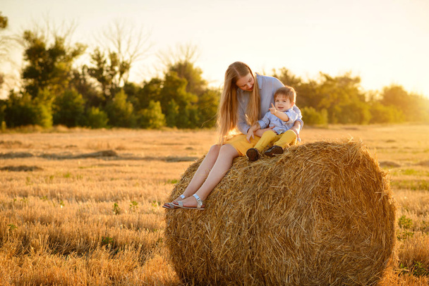 The little lovely boy and his sister in the field with straw sheaves - Zdjęcie, obraz