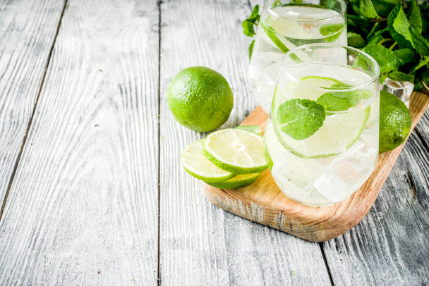 Summer sour drink, with lime and mint, homemade cocktail mojito in two glasses, white wooden background, with fresh limes, mint leaves, ice cubes, copy space - Foto, afbeelding