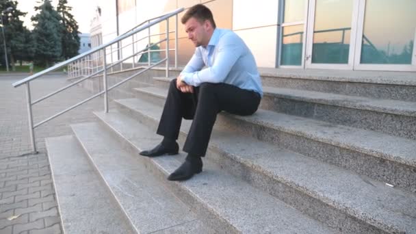 Zbliżenie zdenerwowany smutny Menedżer siedząc na schodach w pobliżu biurowca i płacz. Zdesperowany młody biznesmen dostał bardzo zła wiadomość na telefon i uczucie rozpaczy odkryty. Koncepcja kryzysu finansowego - Materiał filmowy, wideo