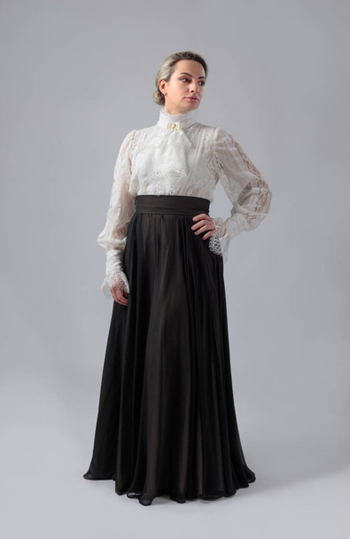 Naisen muotokuva viktoriaanisissa vaatteissa. Valkoinen pusero pitsi, kirjonta ja korkea kaulus. Pitkä kerroksellinen hame leveällä vyöllä
. - Valokuva, kuva