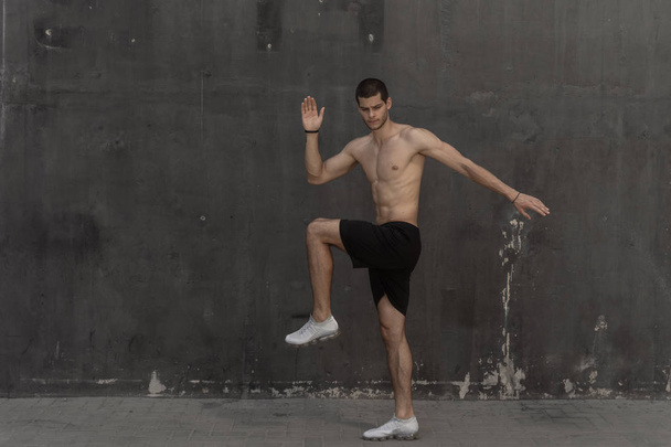 Νεαρός αθλητής άνθρωπος, γυμνό κορμό, τρέχει σε φόντο γκρίζο τοίχο. - Φωτογραφία, εικόνα