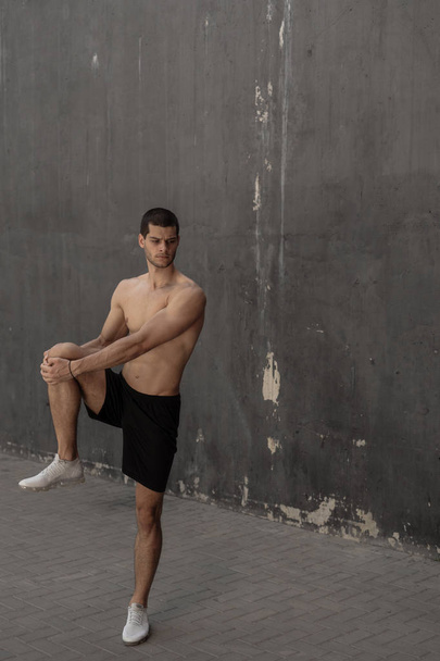 Handsome, athletic man warming up stretching before the training, with gray walls in the background. Healthy lifestyle and sportswear advertising. - Фото, зображення